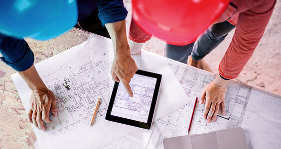 Planer mit Tablet auf Bauplänen in der Baustelle